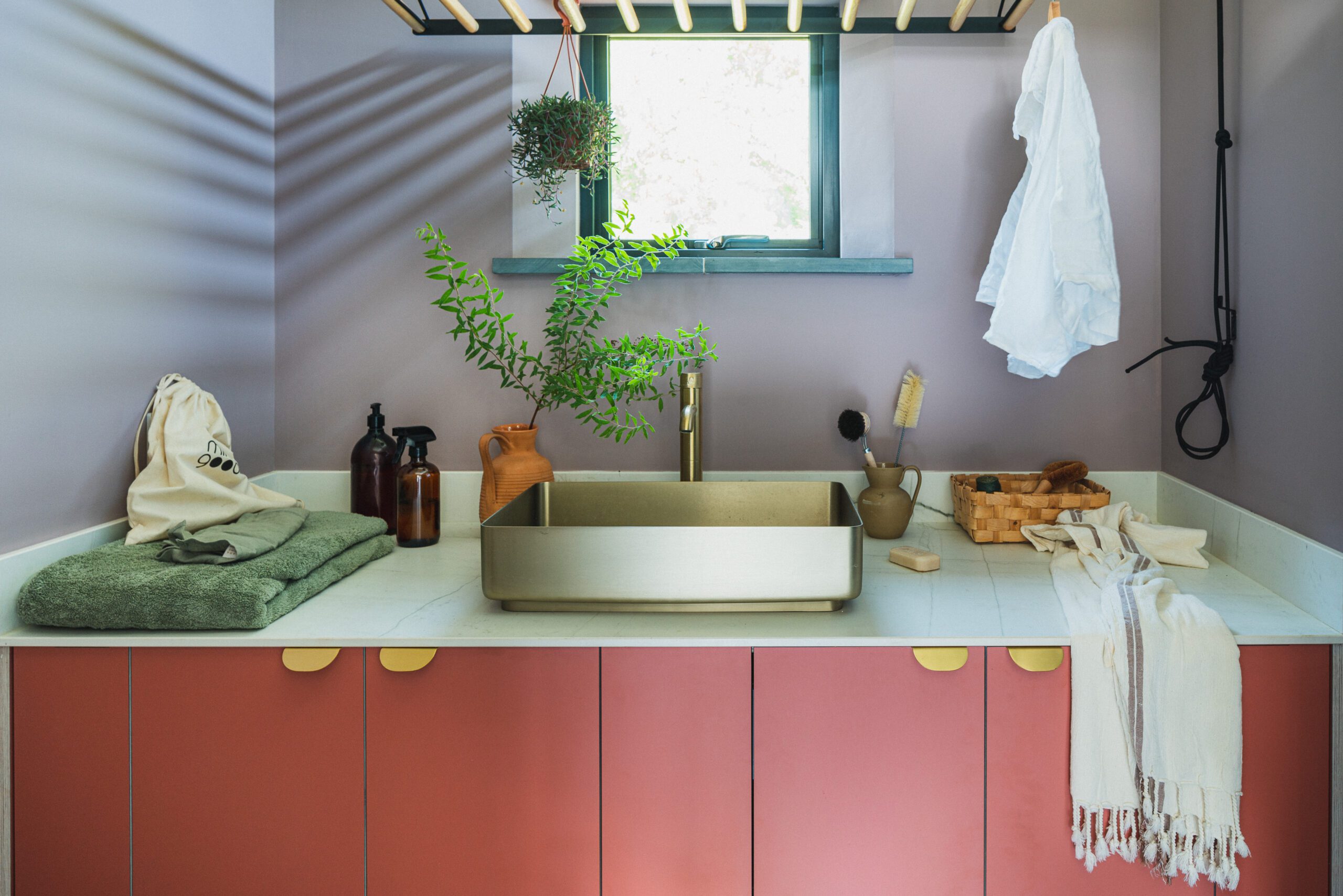 The utility room in Made by HUSK's Goldney Lodge Kitchen, featuring pink fronts and an off white worktop.