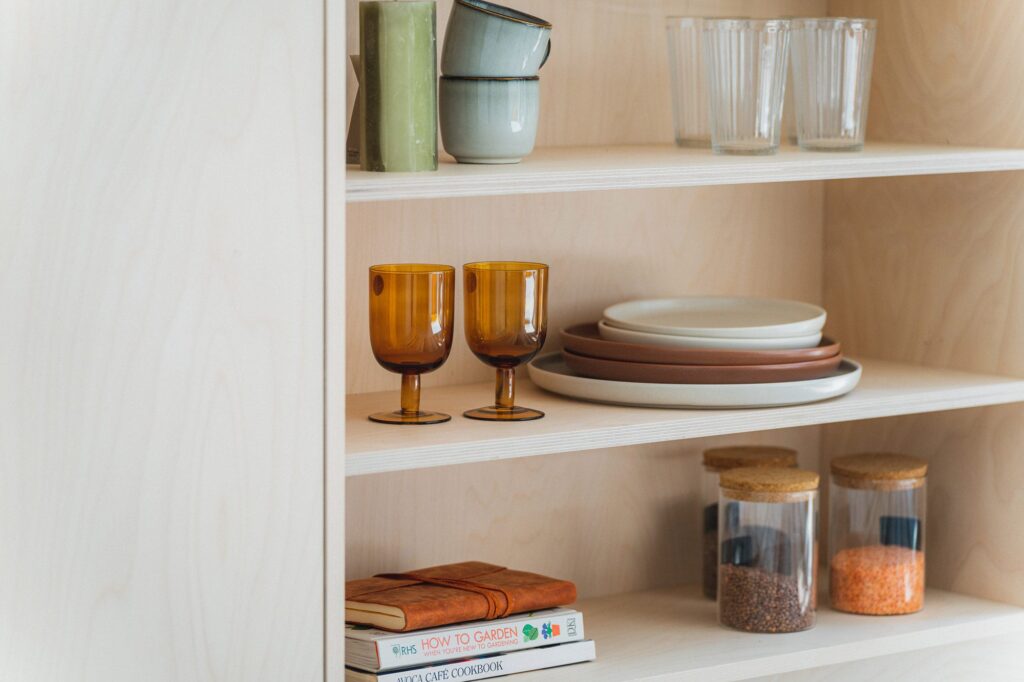 Styled kitchen shelf with ceramics, glassware and books in warm earthy tones, adding texture and character to a low-light kitchen.