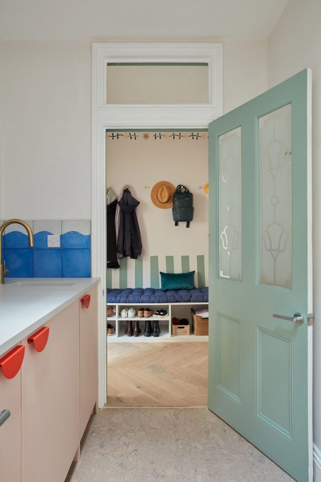 HUSK light pink kitchen with red cabinet handles, blue and white tiles and duck egg blue door leading to the hallway.