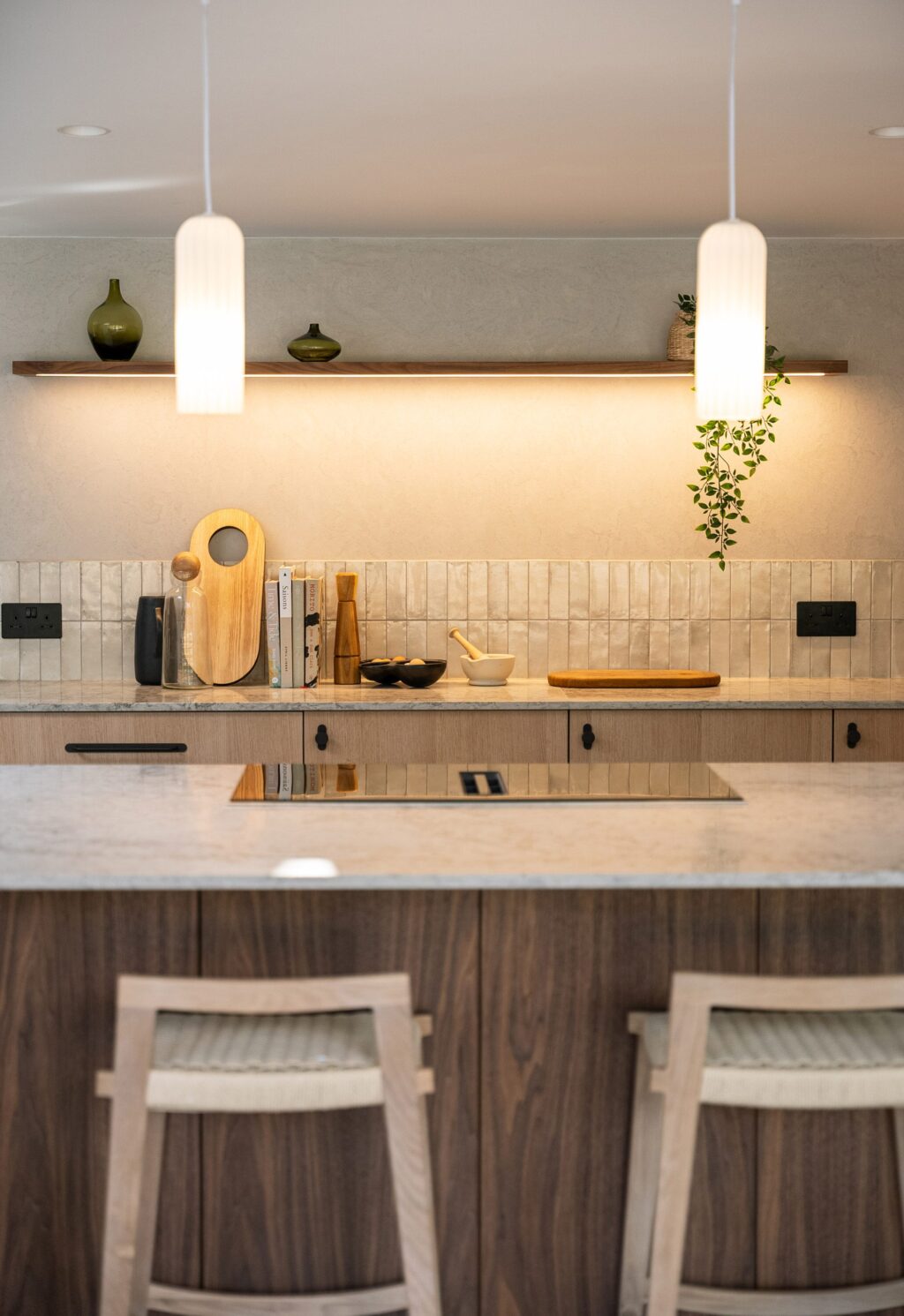 North-facing kitchen with wooden cabinetry and composite stone worktop, showing warm lighting over island and under shelves.