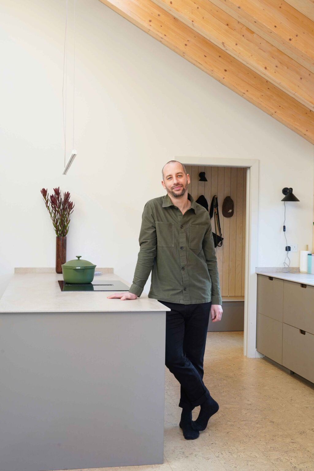 Man in a green shirt standing against a grey kitchen island in a kitchen with white walls.