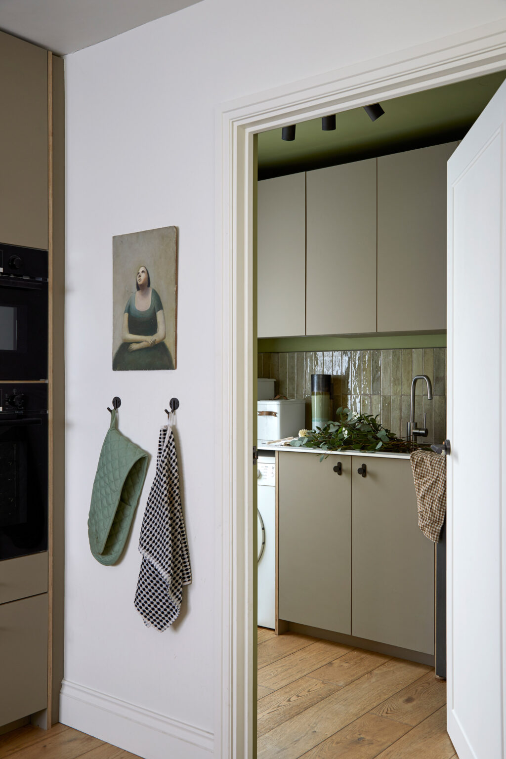 Through a doorway to the side of the kitchen is the matching utility room with earthy green cabinet fronts, rustic metro tiles and deep green walls.