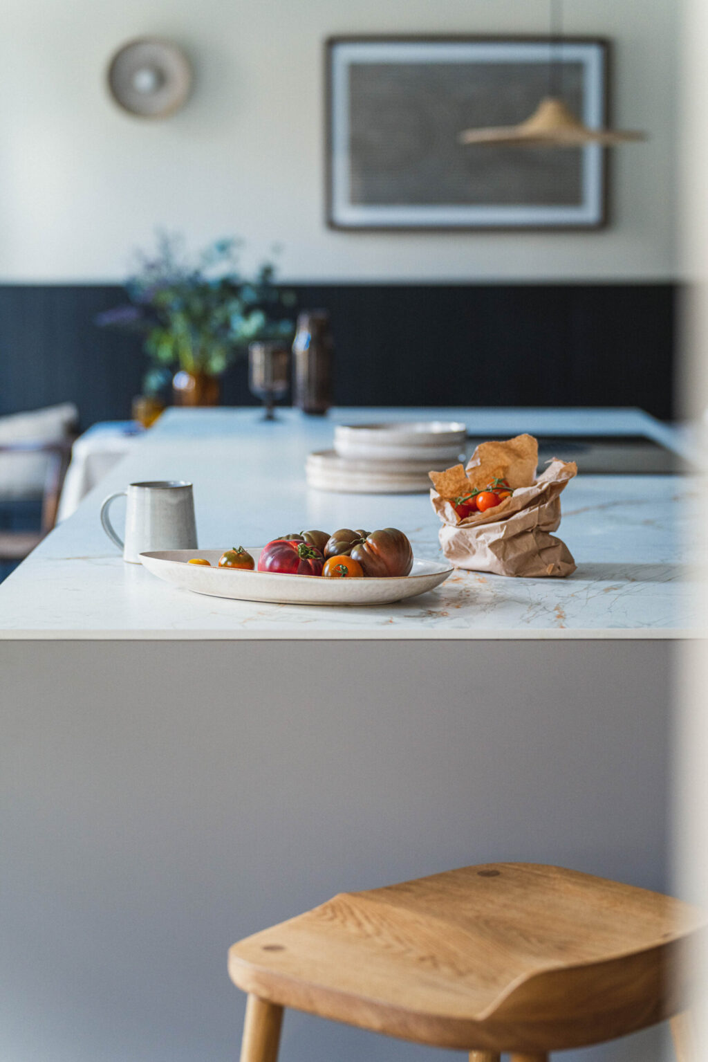 The side of a grey kitchen island that has a plate of tomatoes on and a wooden stool next to the island