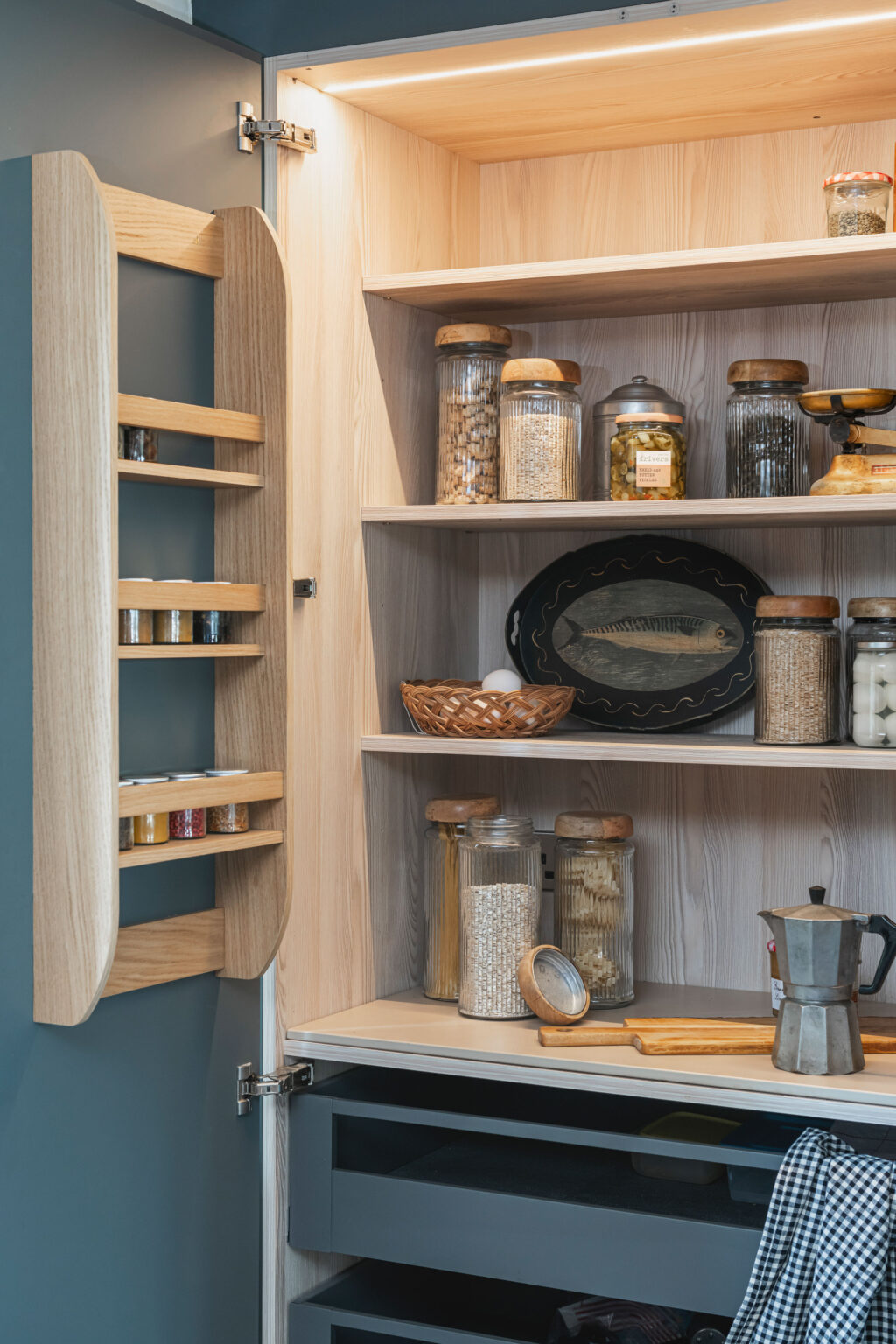 A blue and wooden larder with kitchenware and jarred dried food on the wooden shelves.