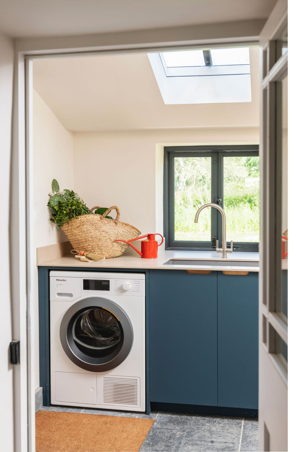A modern utility room with a blue cabinetry under a window, a white washing machine and sink,