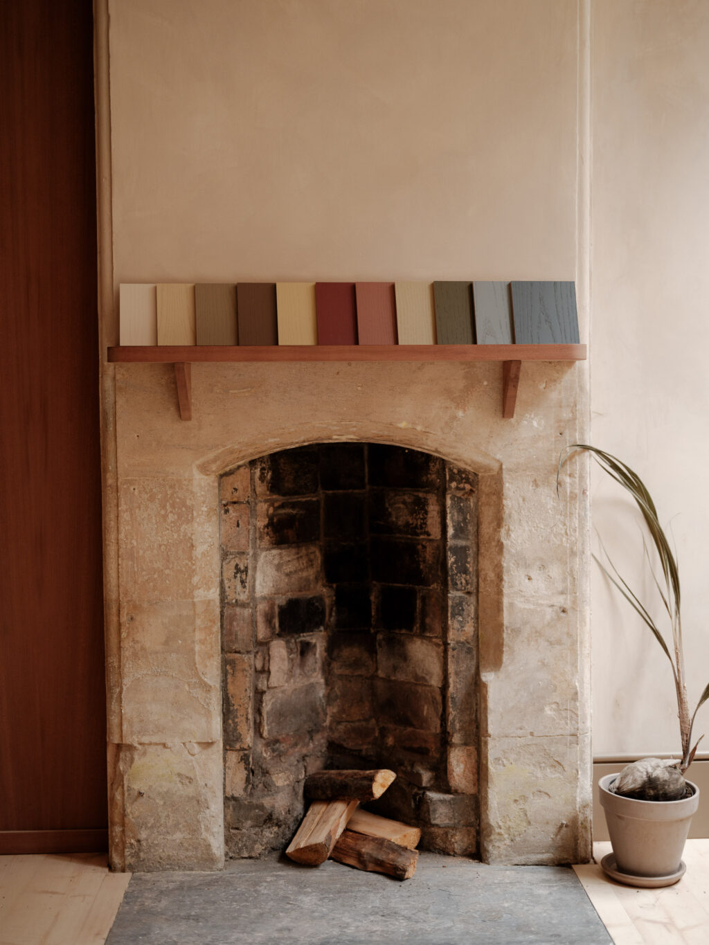 HUSK x Ro Projects - 11 painted shades of crown ash veneer samples displayed in a row on a shelf above an old fireplace.