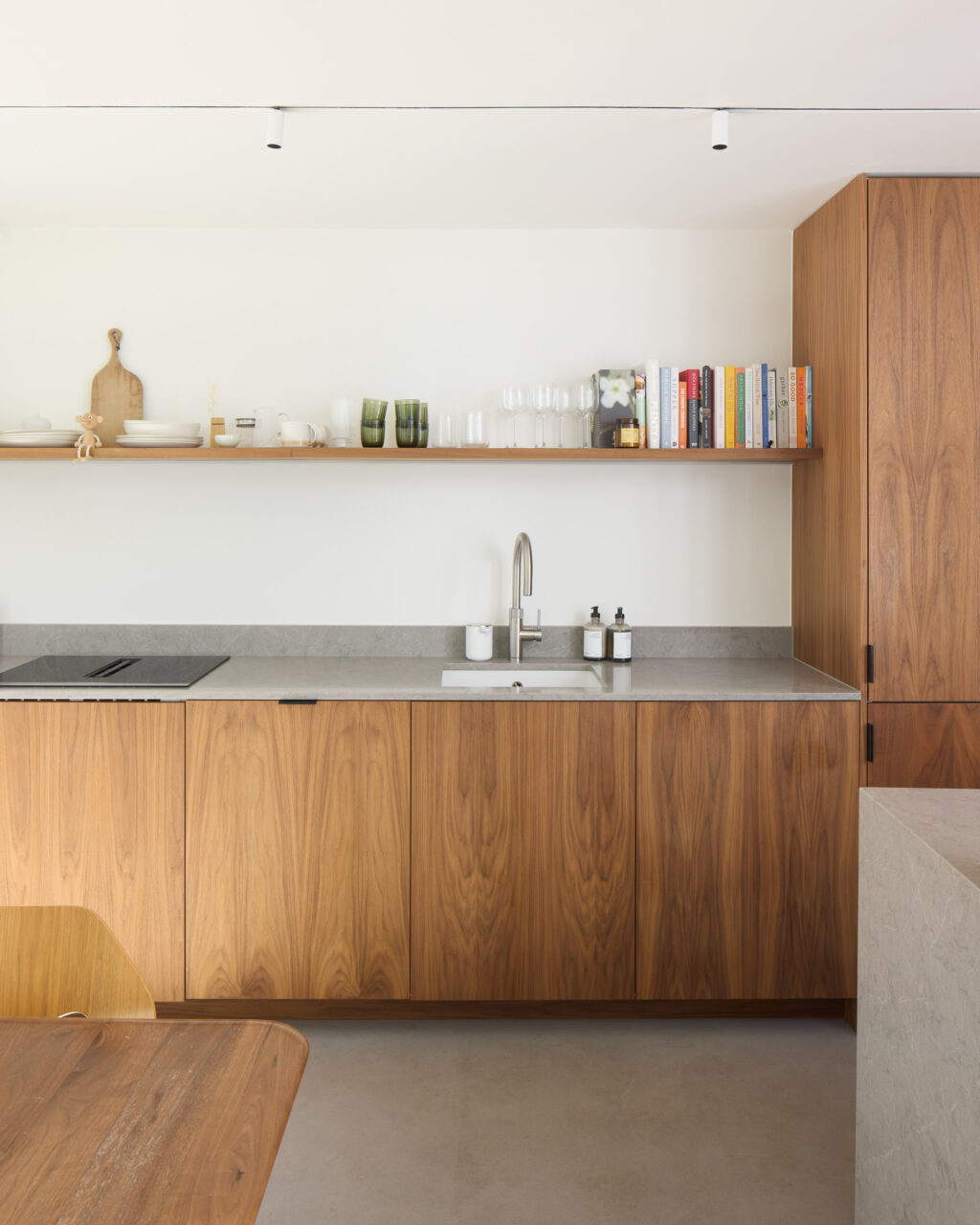 Detail of walnut kitchen cabinetry and open shelf with glassware, books, and kitchen objects.