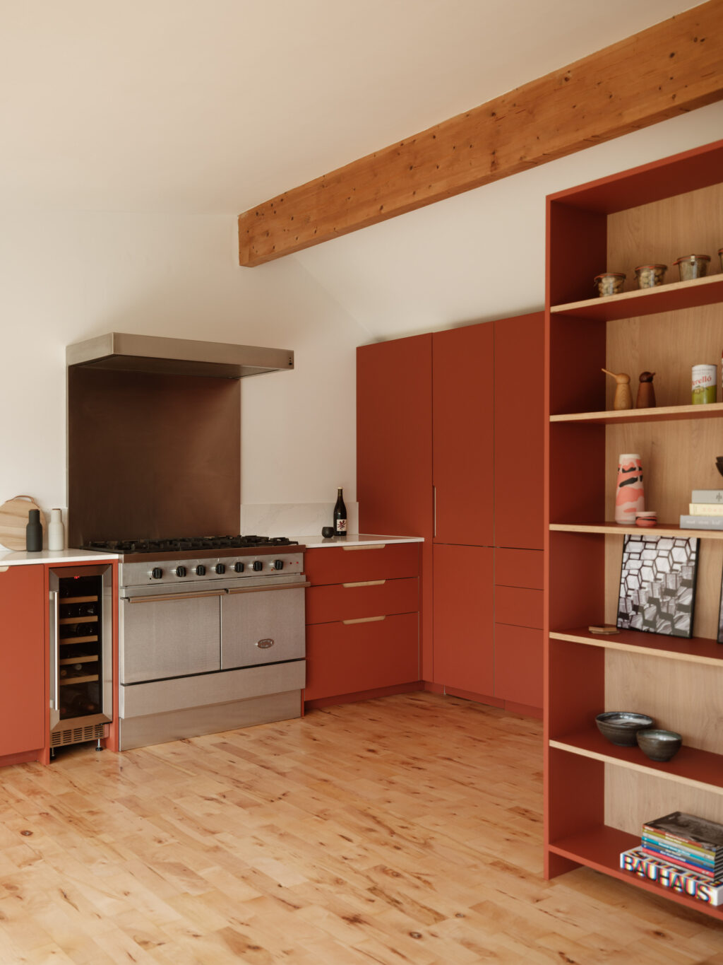 Kitchen corner with a stainless steel range, wine fridge, and terracotta cabinetry paired with light stone countertops.