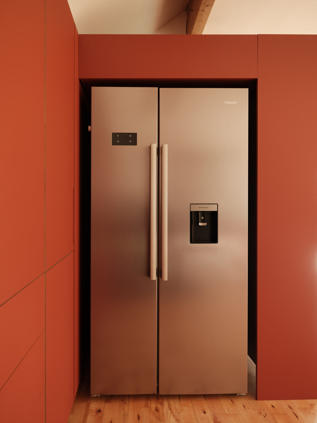 Freestanding stainless steel fridge freezer recessed within terracotta cabinetry in a warm-toned kitchen.