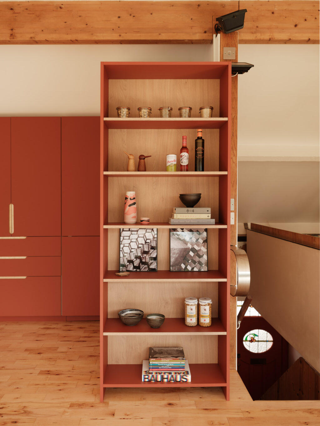 Tall open shelving unit in terracotta finish with oak interior, styled with jars, books, ceramics, and bottles.
