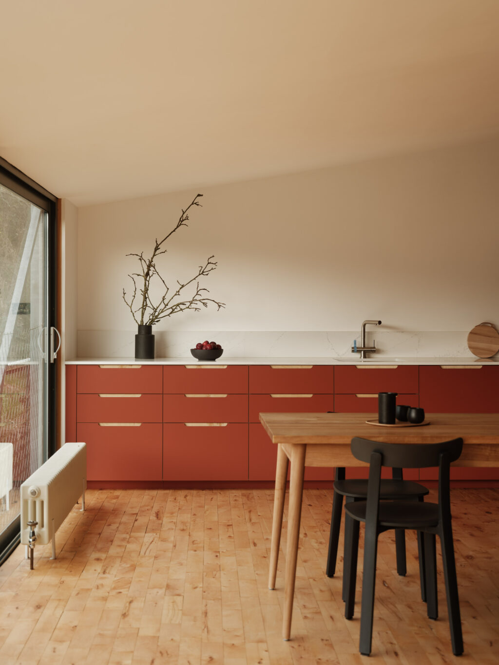 Wide kitchen view with terracotta base cabinets, white worktop, branch arrangement, and wooden dining table.