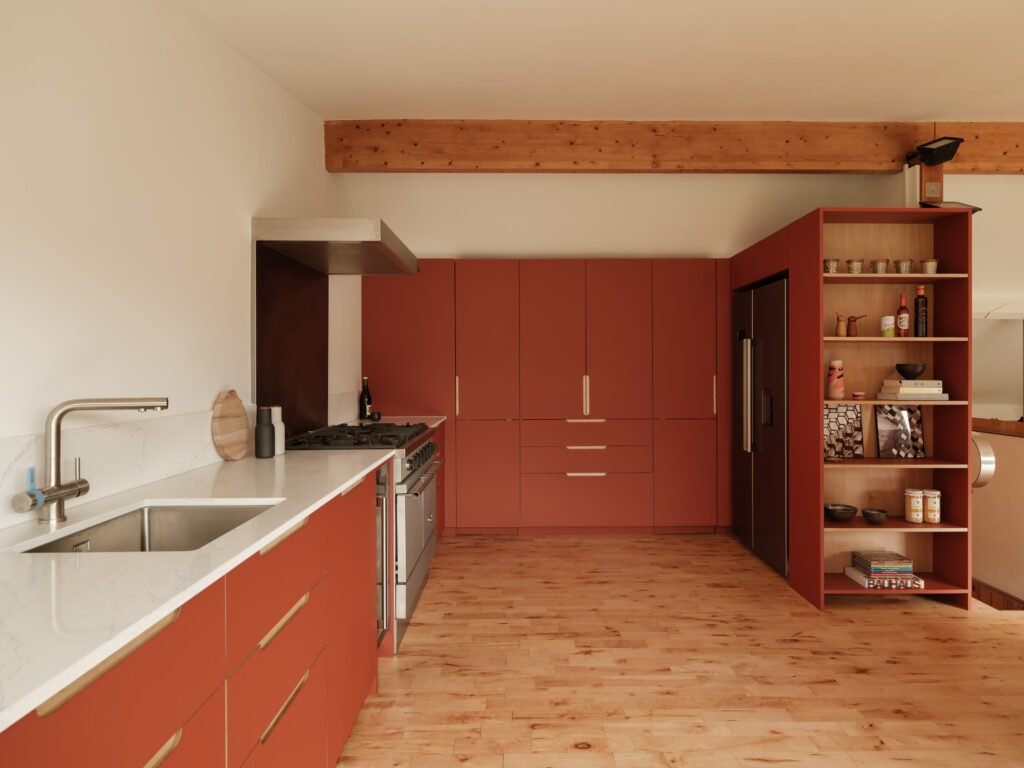Wide kitchen view with sink, hob, stainless steel range, and terracotta cabinetry beneath a wooden beam.