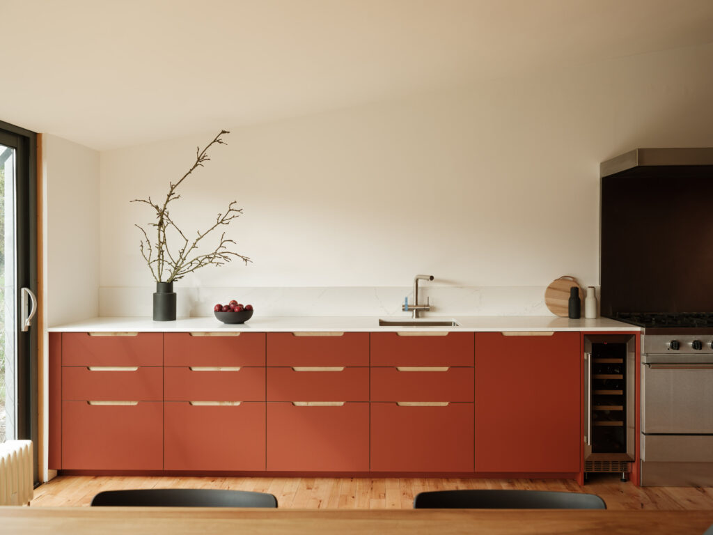 Long run of terracotta base cabinets with scallop handles, white worktop, sink, and decorative branches.
