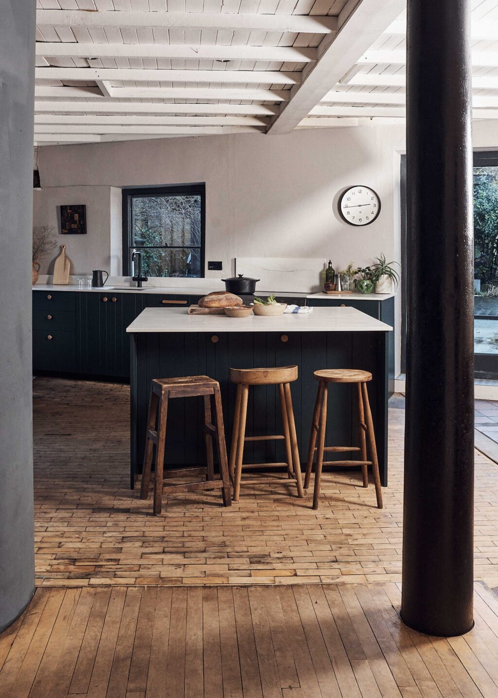Wide view of bespoke dark green ash veneer kitchen with marble island, wooden stools and rustic flooring, handcrafted by Made by HUSK