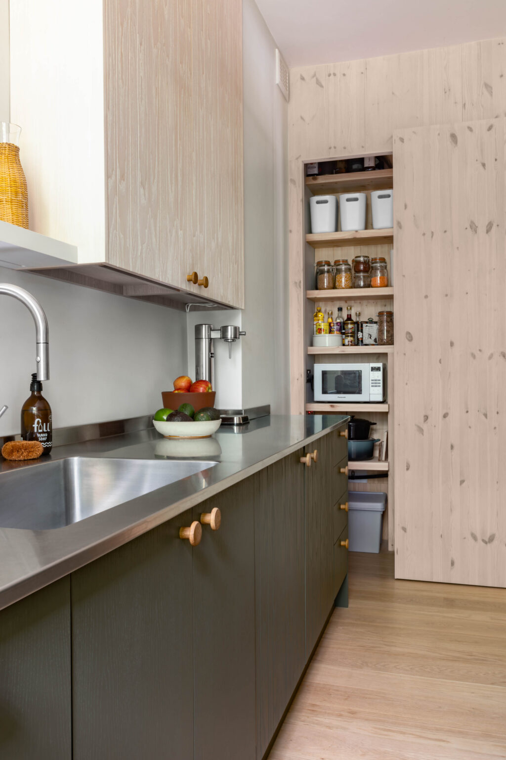 Contemporary ash veneer kitchen with integrated pantry storage, stainless steel worktop, and handcrafted cabinetry by Made by HUSK