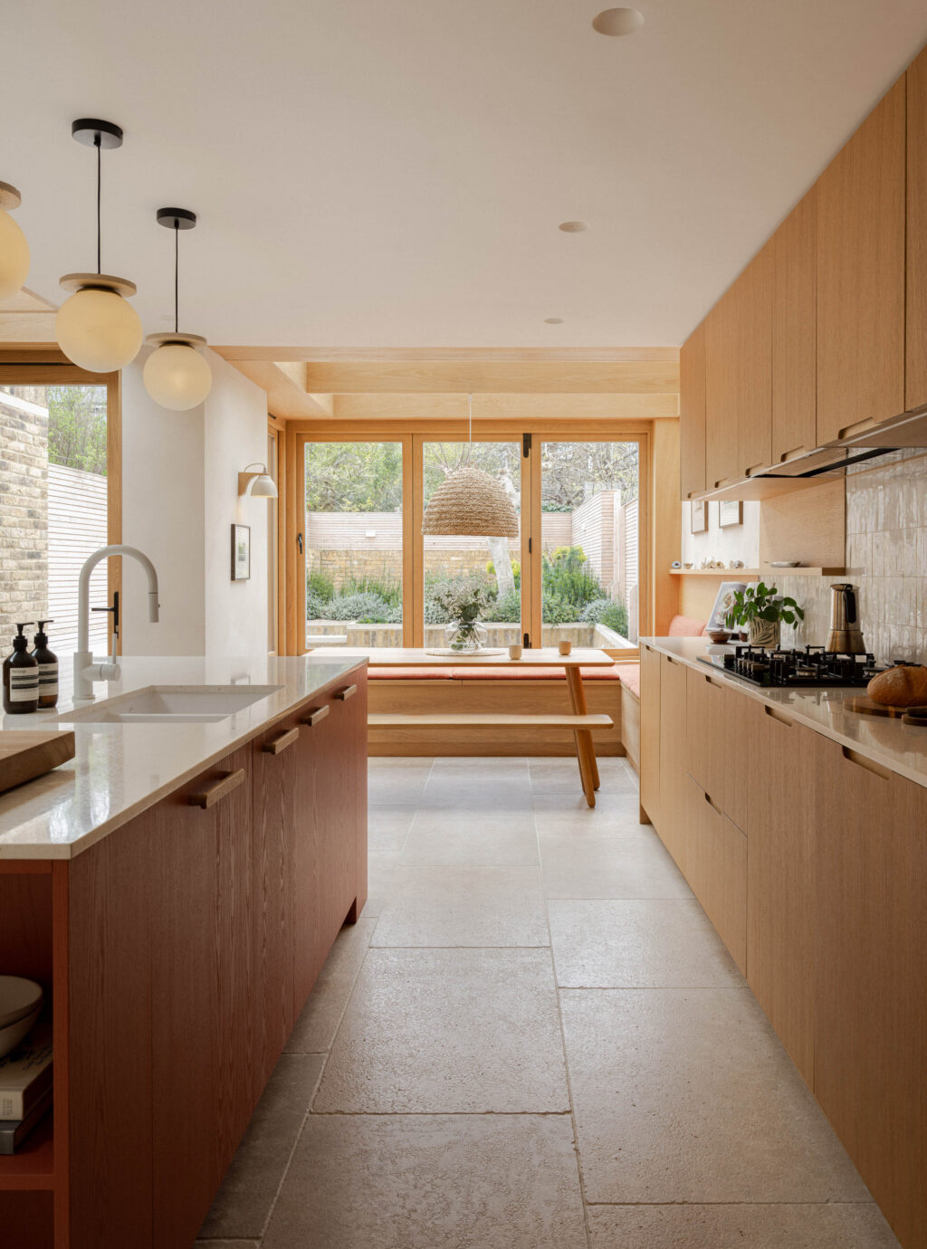 Long kitchen run with oak veneer cabinetry, Devon Red island and built-in oak banquette seating beside large garden windows
