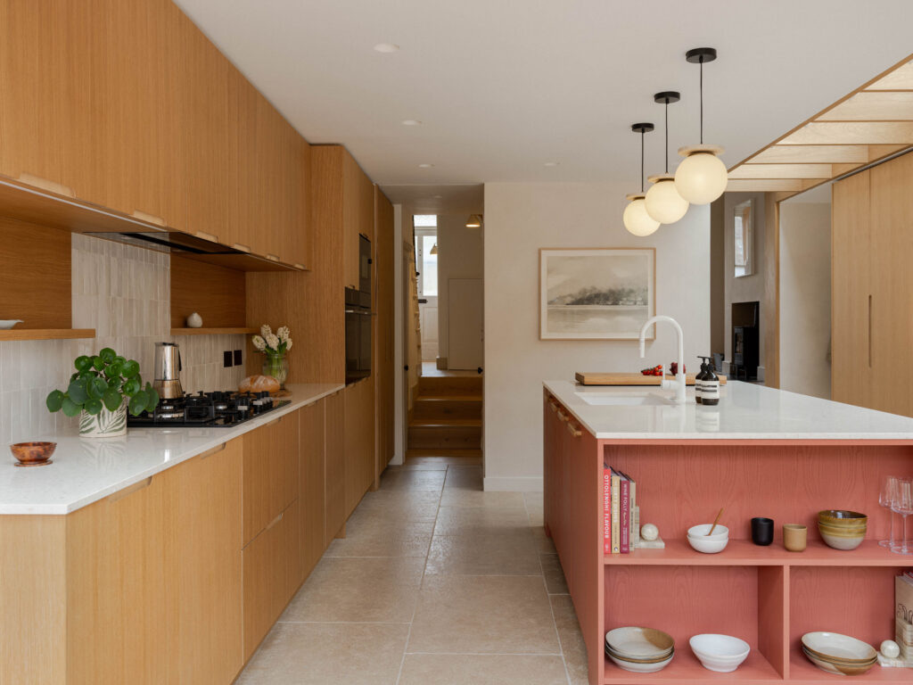 Large kitchen with Natural Oak Veneer cabinetry, HUSK x Another Country Devon Red Fallow island shelving, bright terrazzo surfaces and globe pendant lighting