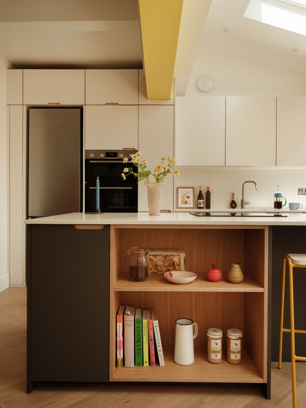 Natural oak open bookcase integrated into the kitchen island, paired with FENIX Grigio Aragona cabinetry, exposed ply scallop handles and a Neolith Just White worktop.