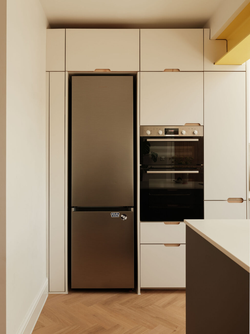 Tall FENIX Bianco Male cabinetry incorporating bespoke fridge bridge cabinets, exposed ply scallop handles and integrated appliance housing.