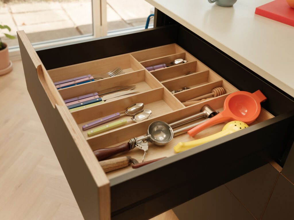 Internal drawer storage with timber cutlery organiser accessory set within a FENIX Grigio Aragona kitchen island drawer.