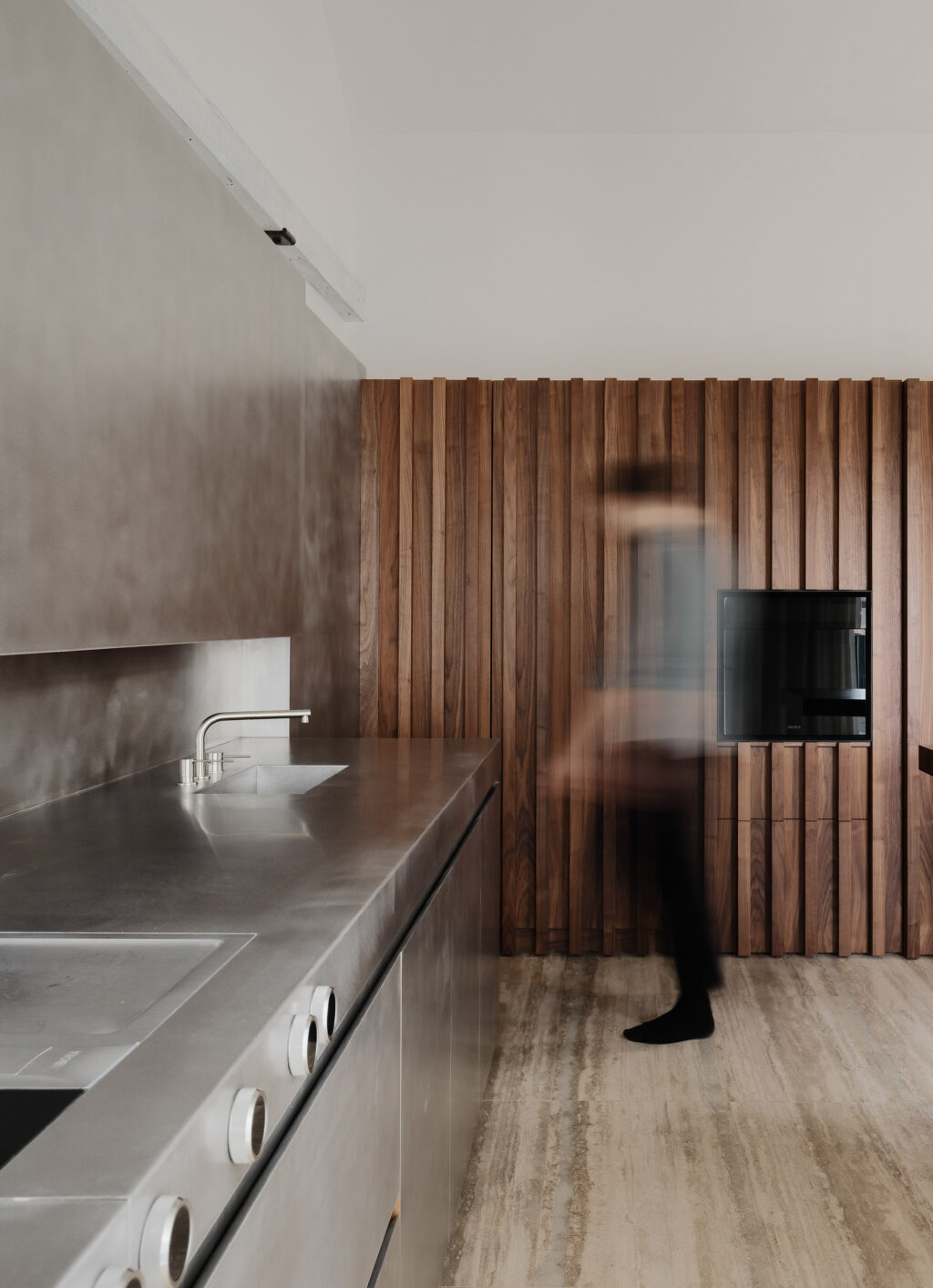 Modern kitchen with a stainless steel worktop, integrated sink and walnut slatted wall panelling creating a warm, contemporary feel.