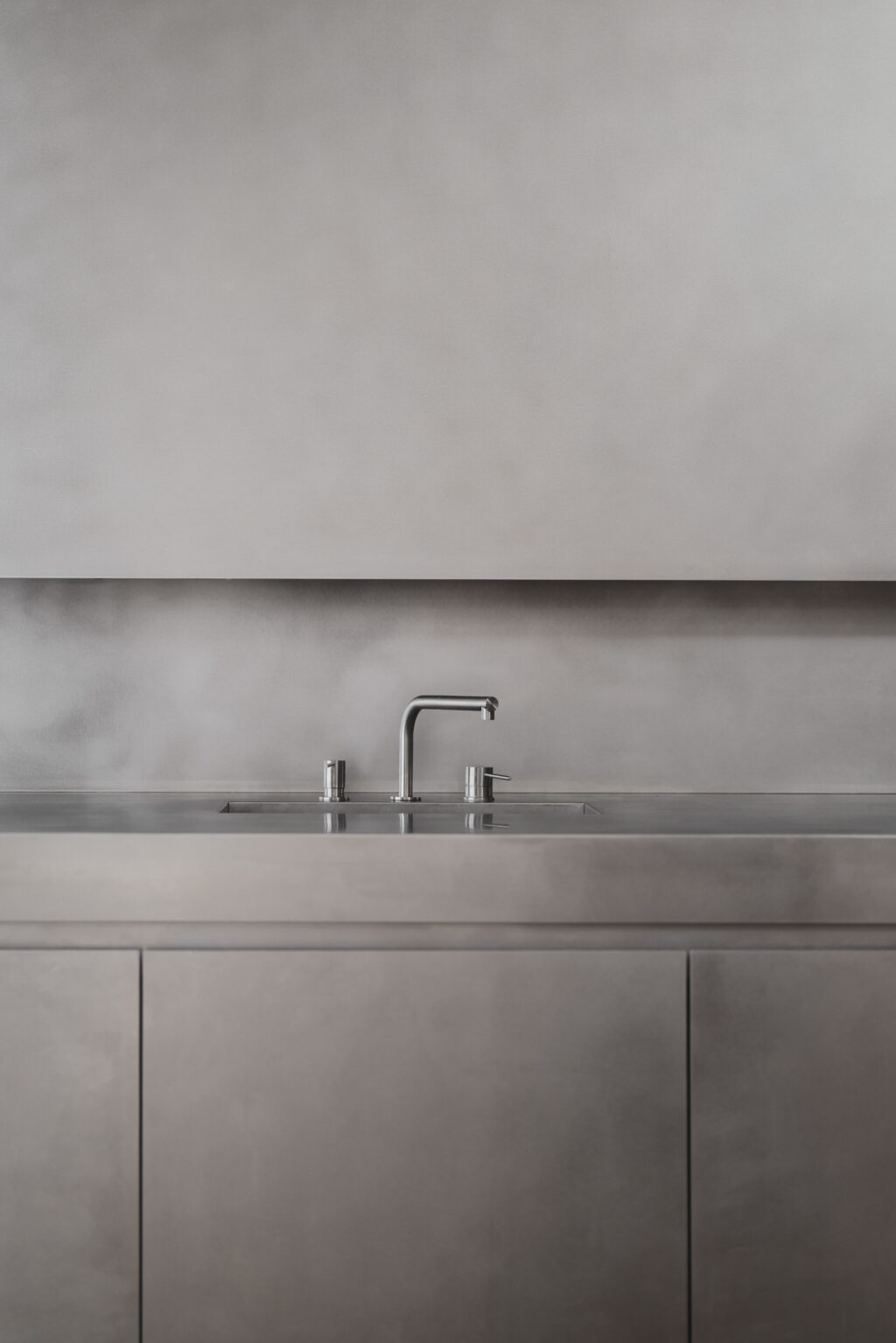 Close-up of a stainless steel worktop with integrated sink and tap, paired with minimalist grey kitchen cabinetry.
