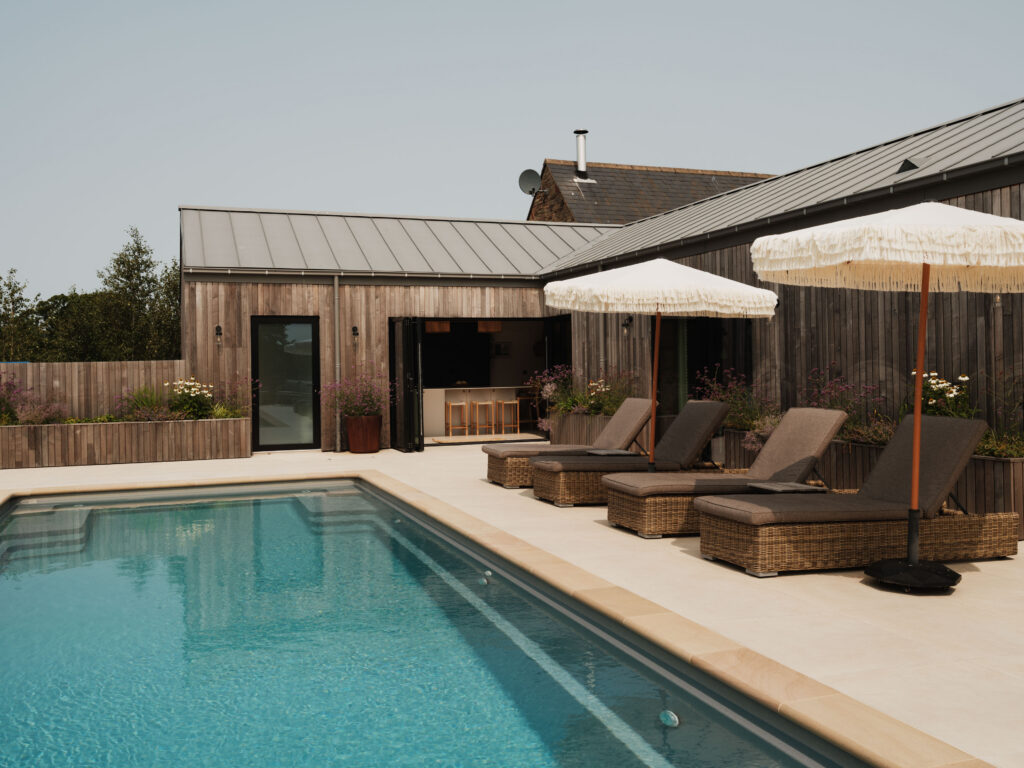 Outdoor swimming pool with sun loungers and parasols overlooking the landscaped garden of The Gloucestershire House.