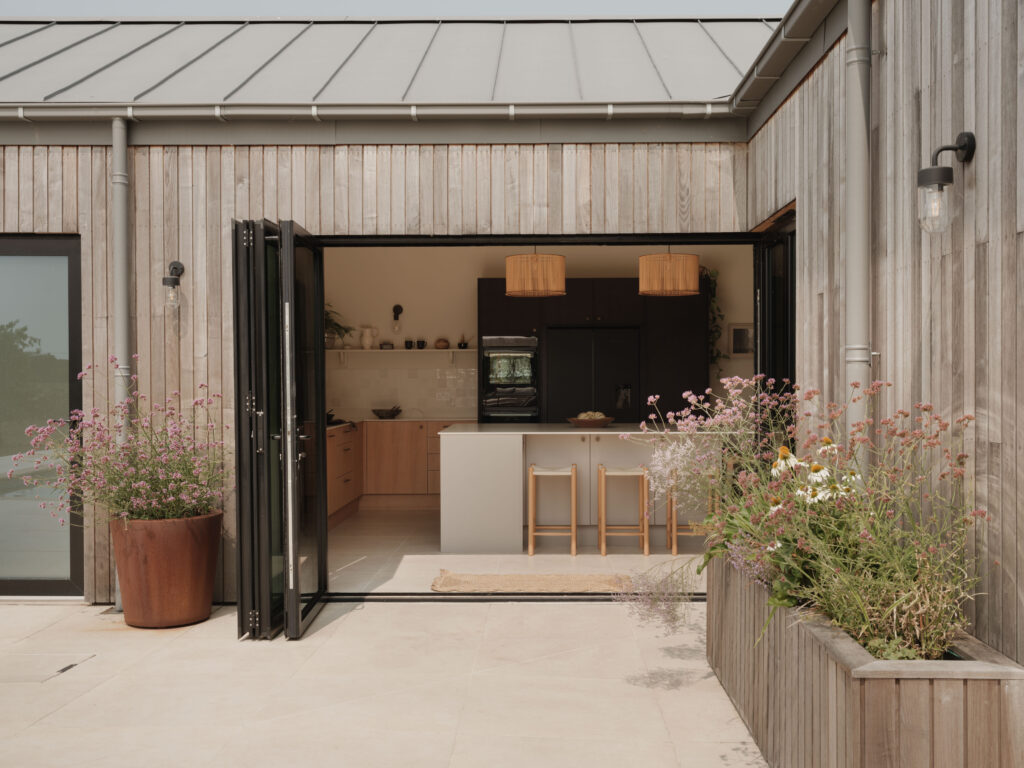 Timber-clad exterior with open bifold doors creating a seamless connection between the HUSK kitchen, terrace and swimming pool.