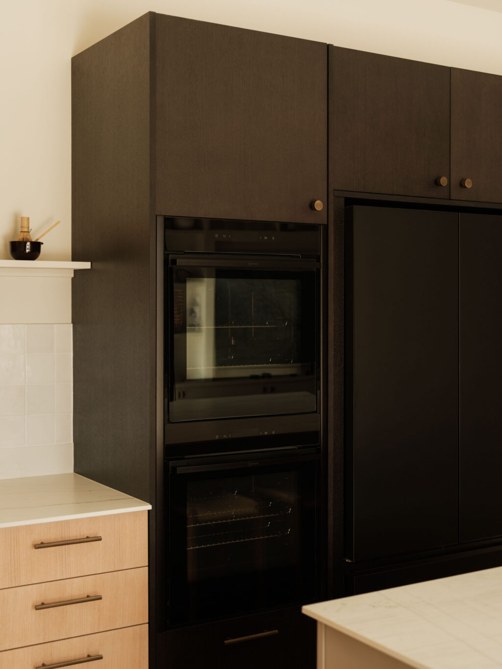 Smoked Oak timber veneer tall cabinets with integrated Fisher & Paykel oven stack and fridge freezer alongside White Tint Oak base cabinetry.