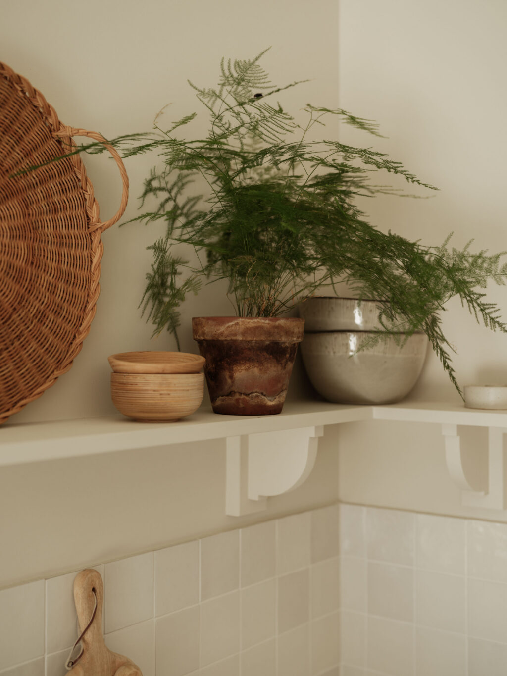 Open painted shelving displaying ceramics and plants above a tiled splashback, complementing the natural materials of The Gloucestershire House kitchen.