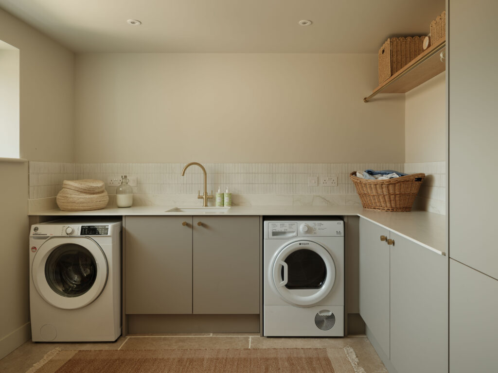 Practical laundry room with FENIX Beige Arizona cabinetry, Neolith Mont Blanc worktops, open shelving and space for washing and drying appliances.