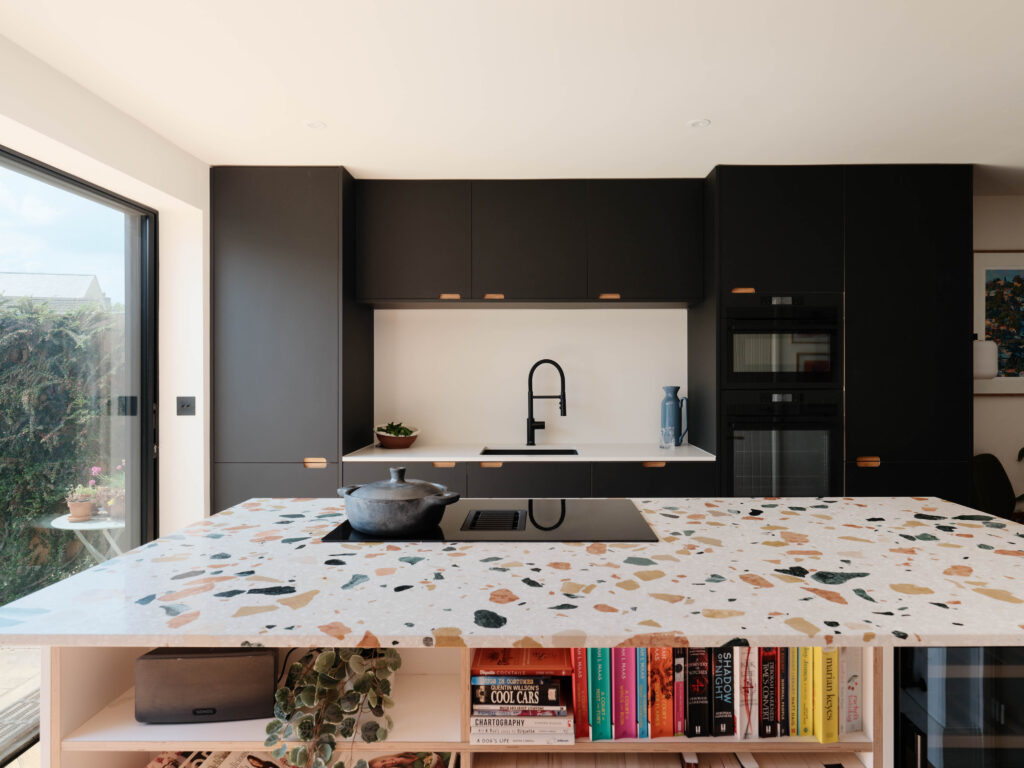 Front view of the terrazzo kitchen island with open bookshelf storage and black cabinetry behind.