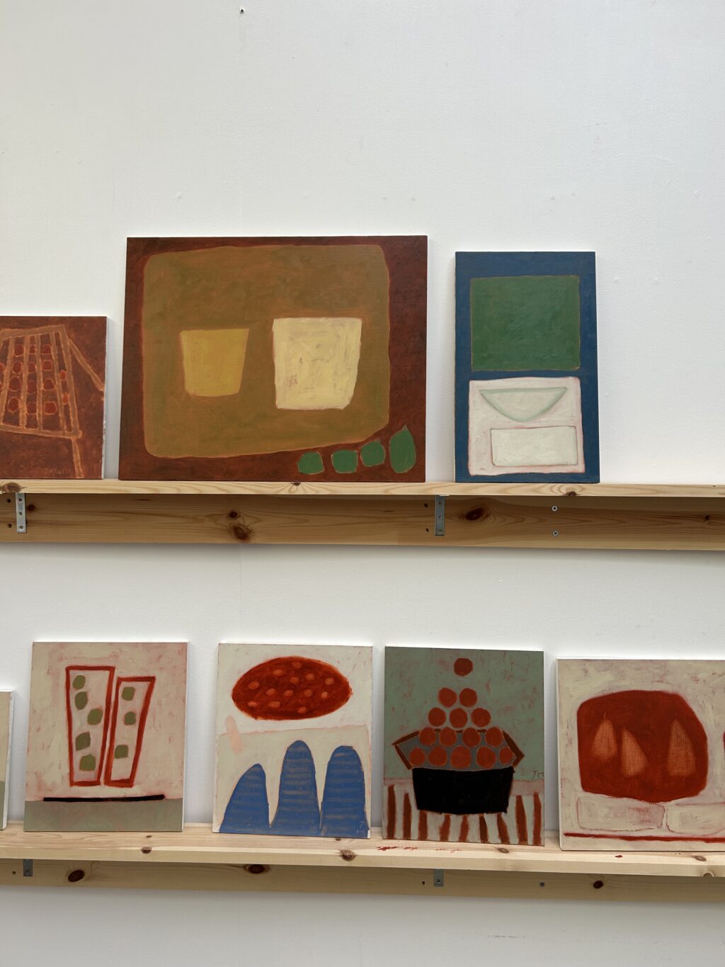 Colourful paintings by Jay Harper arranged across two wooden shelves in her Bristol studio.