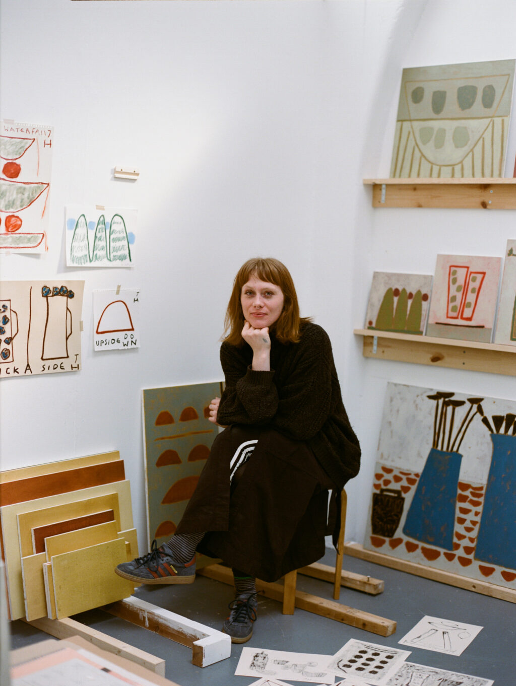 Jay Harper seated in her studio, surrounded by colourful paintings, sketches and works in progress.