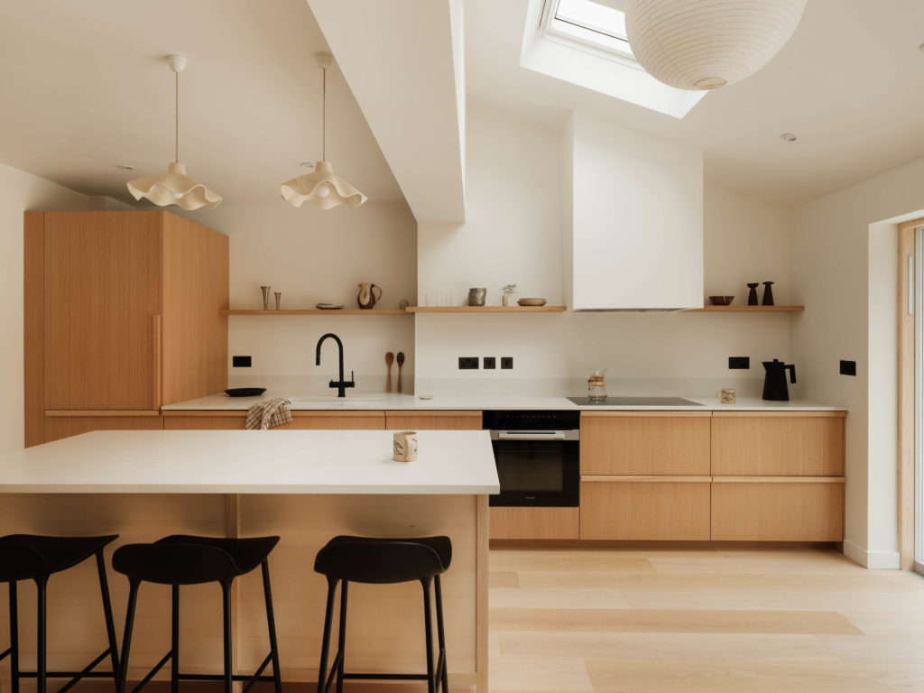 Wide view of the open-plan Beckington Kitchen with Quarter Cut Natural Oak cabinetry, bespoke island, oak shelving and skylights overhead.