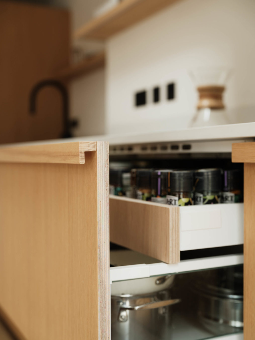 Open oak-fronted kitchen drawer showing the Solid Timber L Handle, exposed ply edge and internal storage.