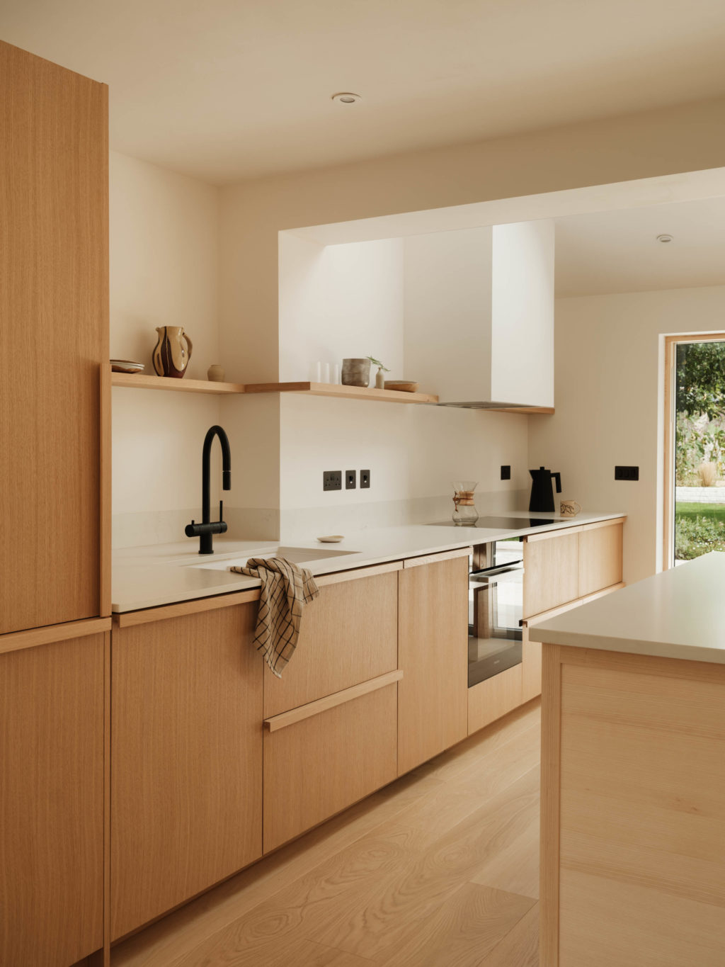 Angled view along the Beckington Kitchen showing Quarter Cut Natural Oak cabinetry, solid oak handles, Dreamy Carrara worktop and open oak shelving.