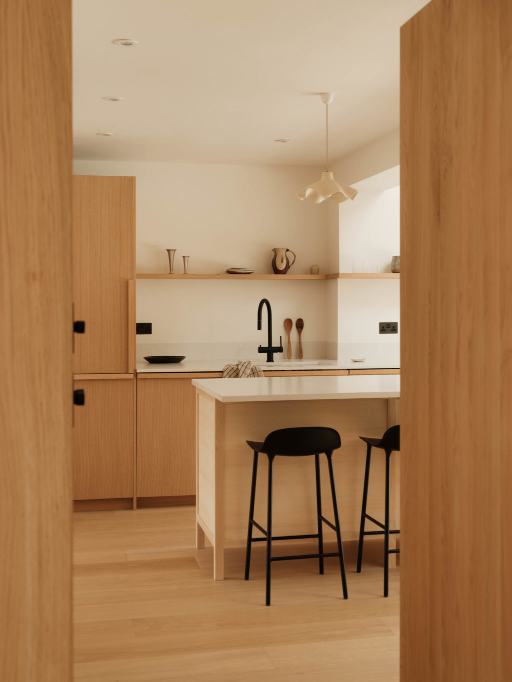 The Beckington Kitchen viewed from the hallway, showing the oak cabinetry, bespoke island with seating and open oak shelving.