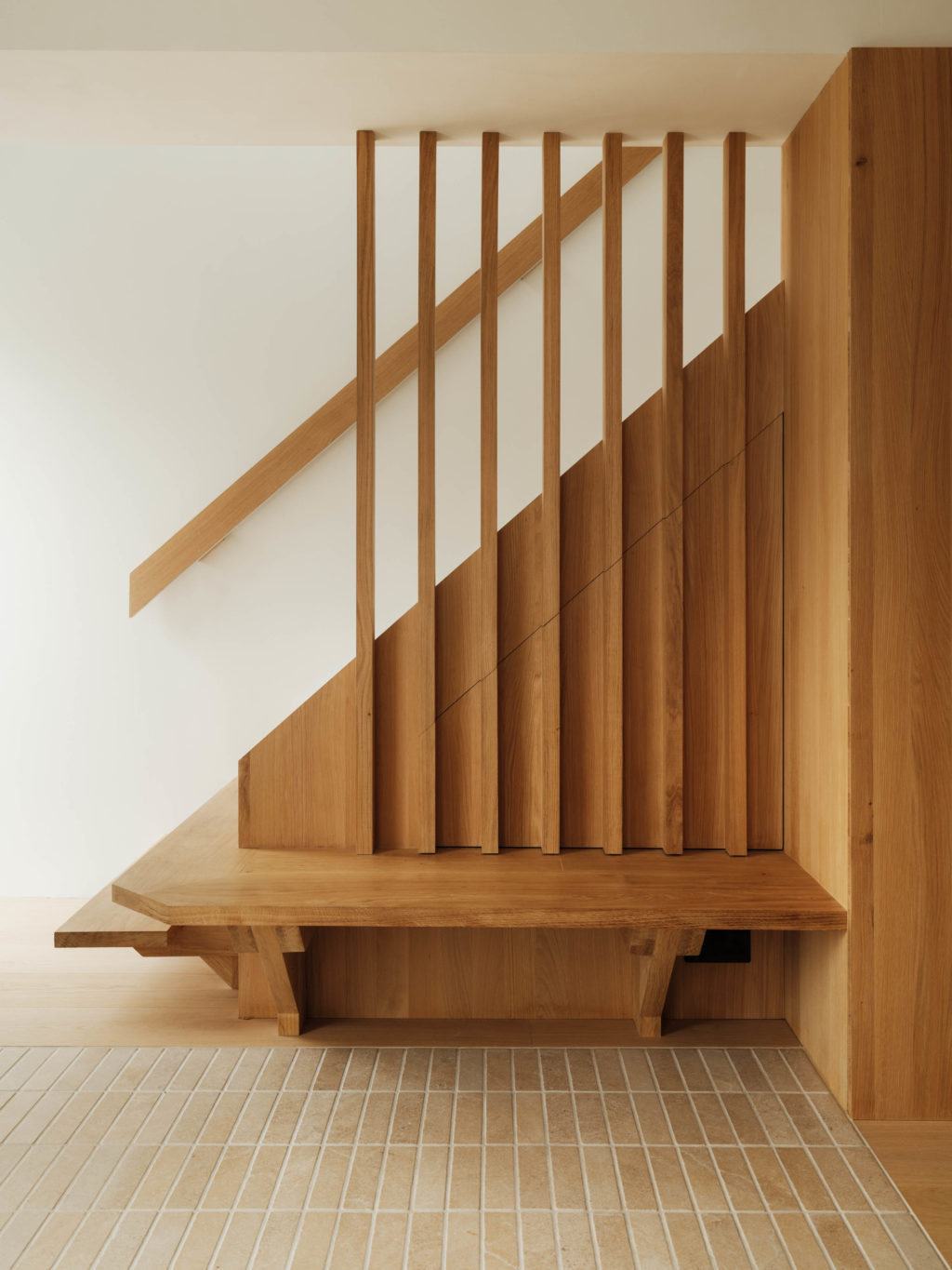 Bespoke oak staircase with vertical timber balustrade, integrated under-stair storage and built-in bench at The Beckington Kitchen project.