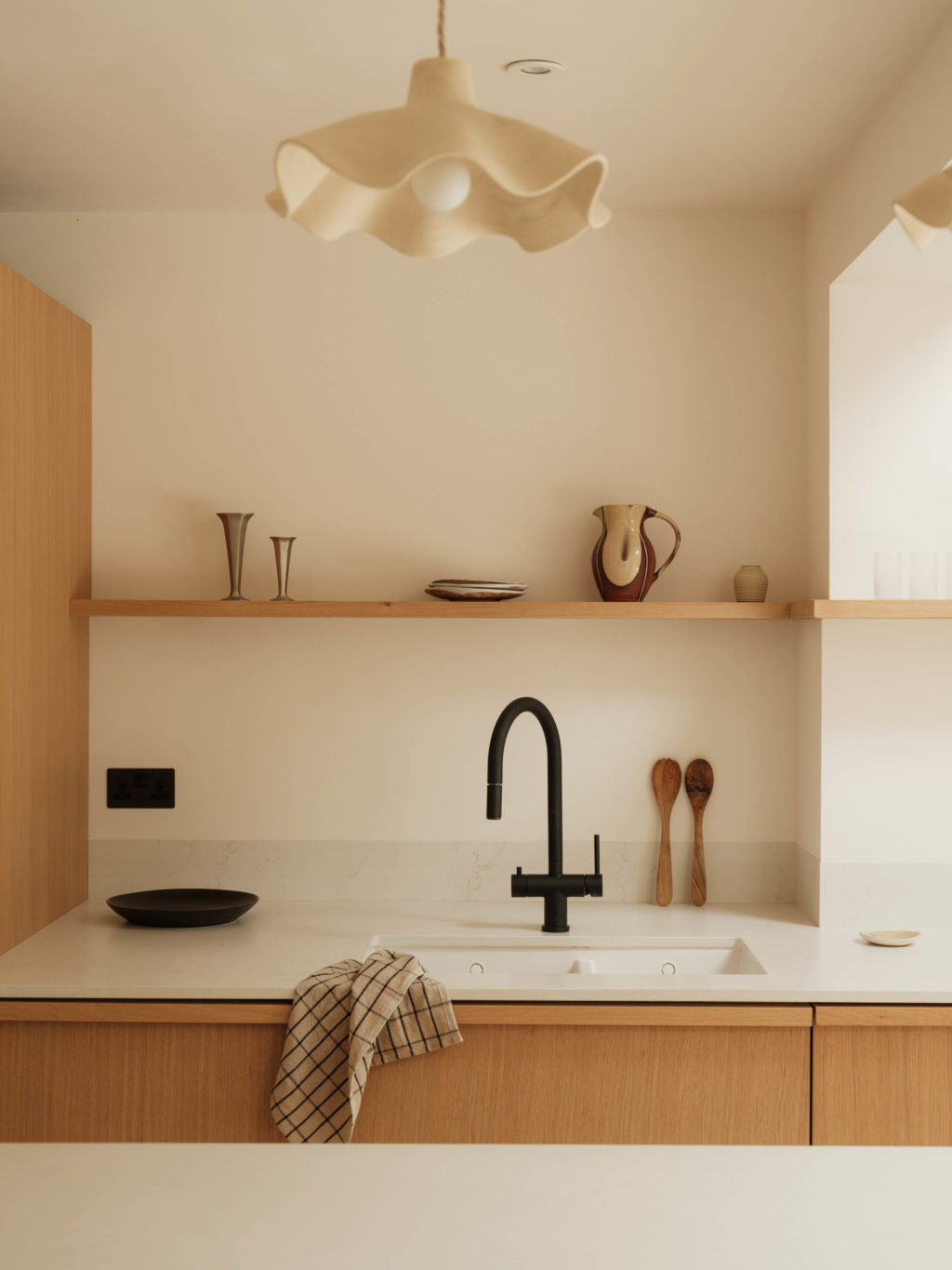 Sink area with Quarter Cut Natural Oak cabinetry, pale worktop, black tap and long open oak shelf styled with ceramics.