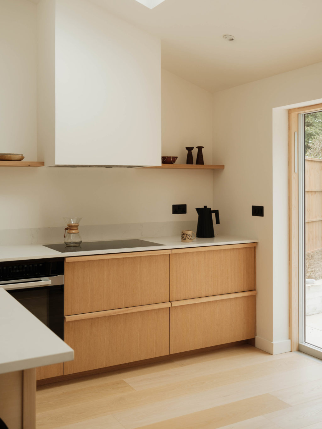 Quarter Cut Natural Oak drawers beside the hob and oven, with pale worktops and open oak shelving in The Beckington Kitchen.