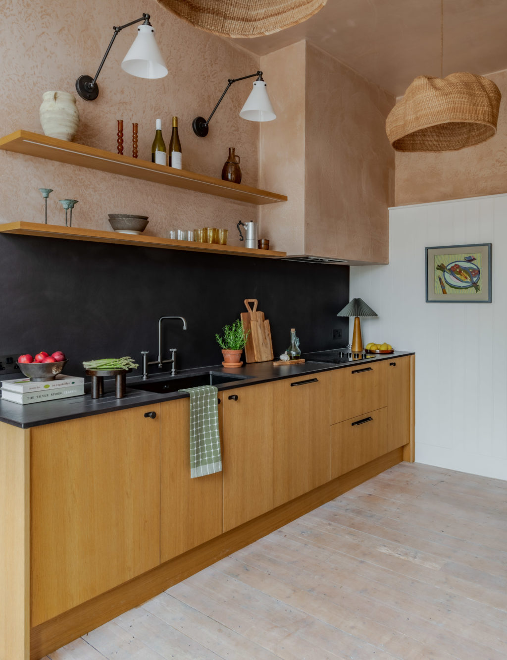 The Piggery kitchen featuring Natural Oak Timber Veneer fronts on Howdens cabinets, black Dekton Sirius worktops, open oak shelving and textured pink plaster walls.